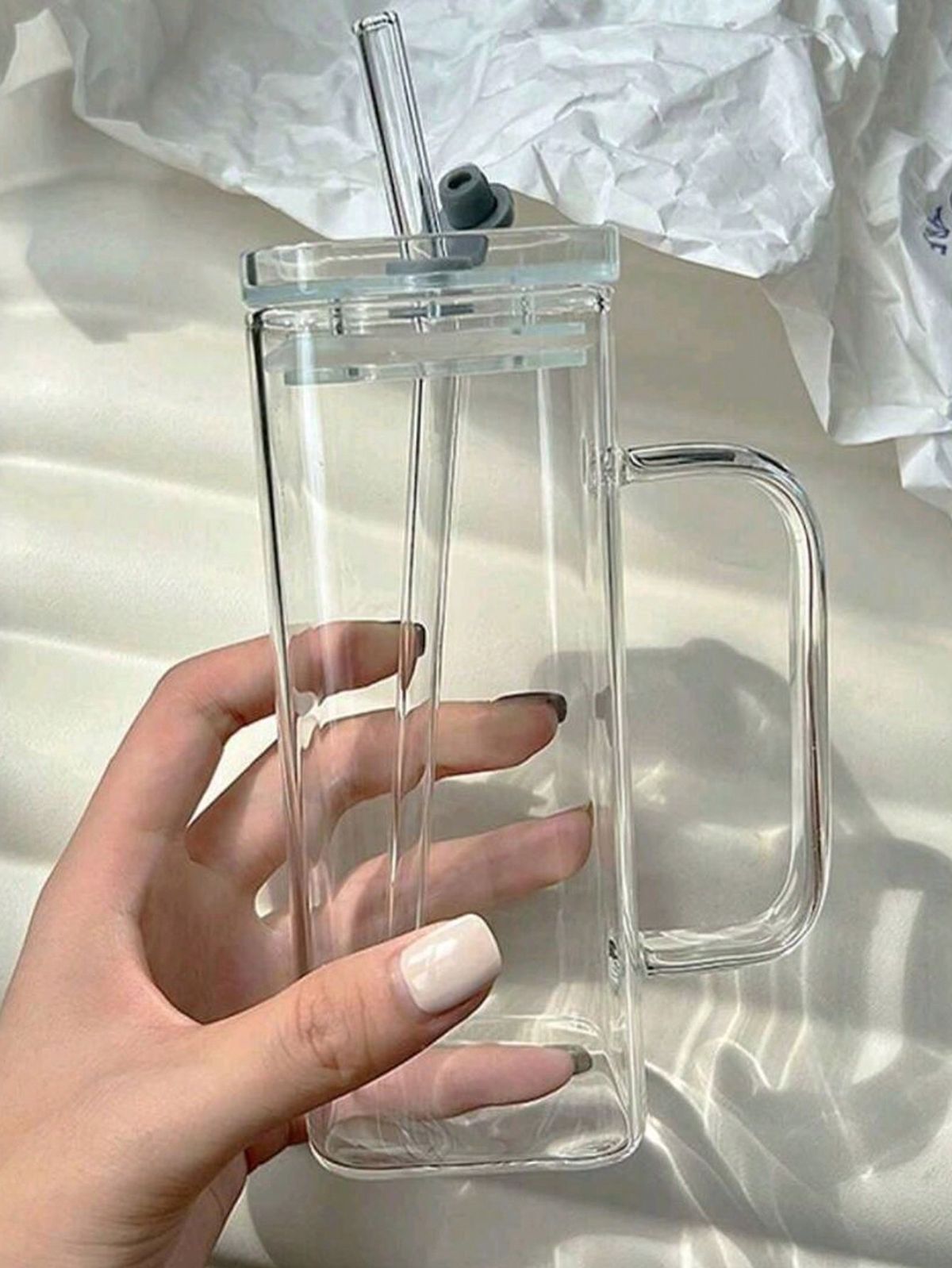 Clear mug with handle and straw held by a hand on a light background