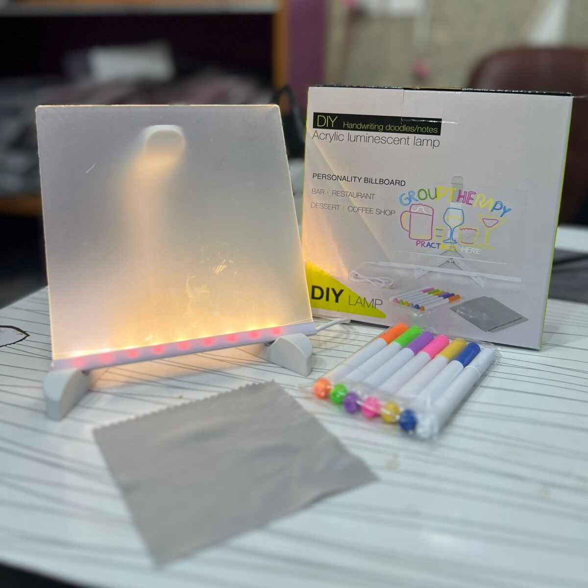 Acrylic LED writing board with colorful glow displaying handwritten message using erasable pens on desk