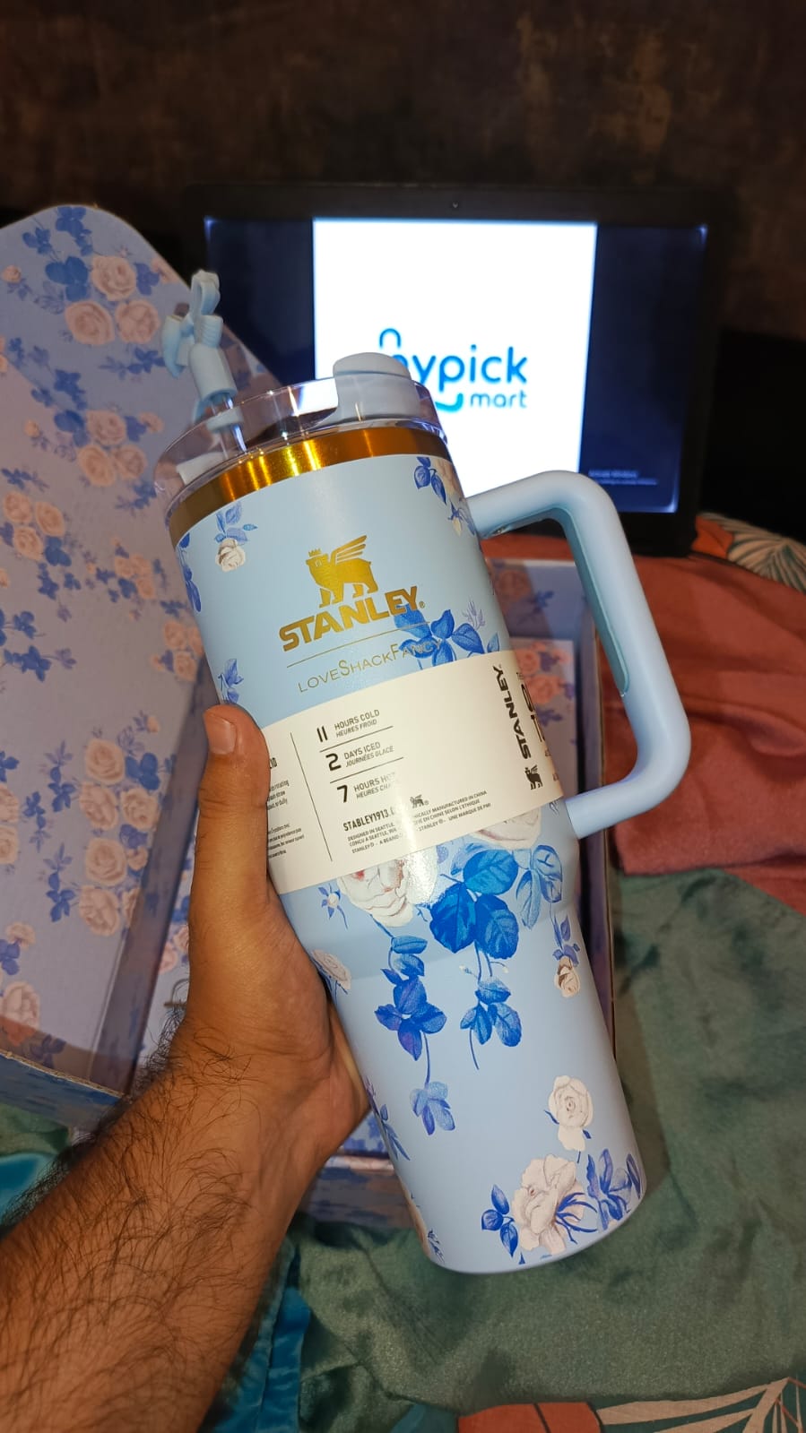 Hand holding a blue Stanley insulated bottle with floral design against a blurred background mypickmart