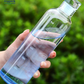 Clear water bottle with measurement markings held by a hand against a green outdoor background