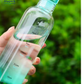 Clear water bottle with green cap held by a hand against a blurred green background