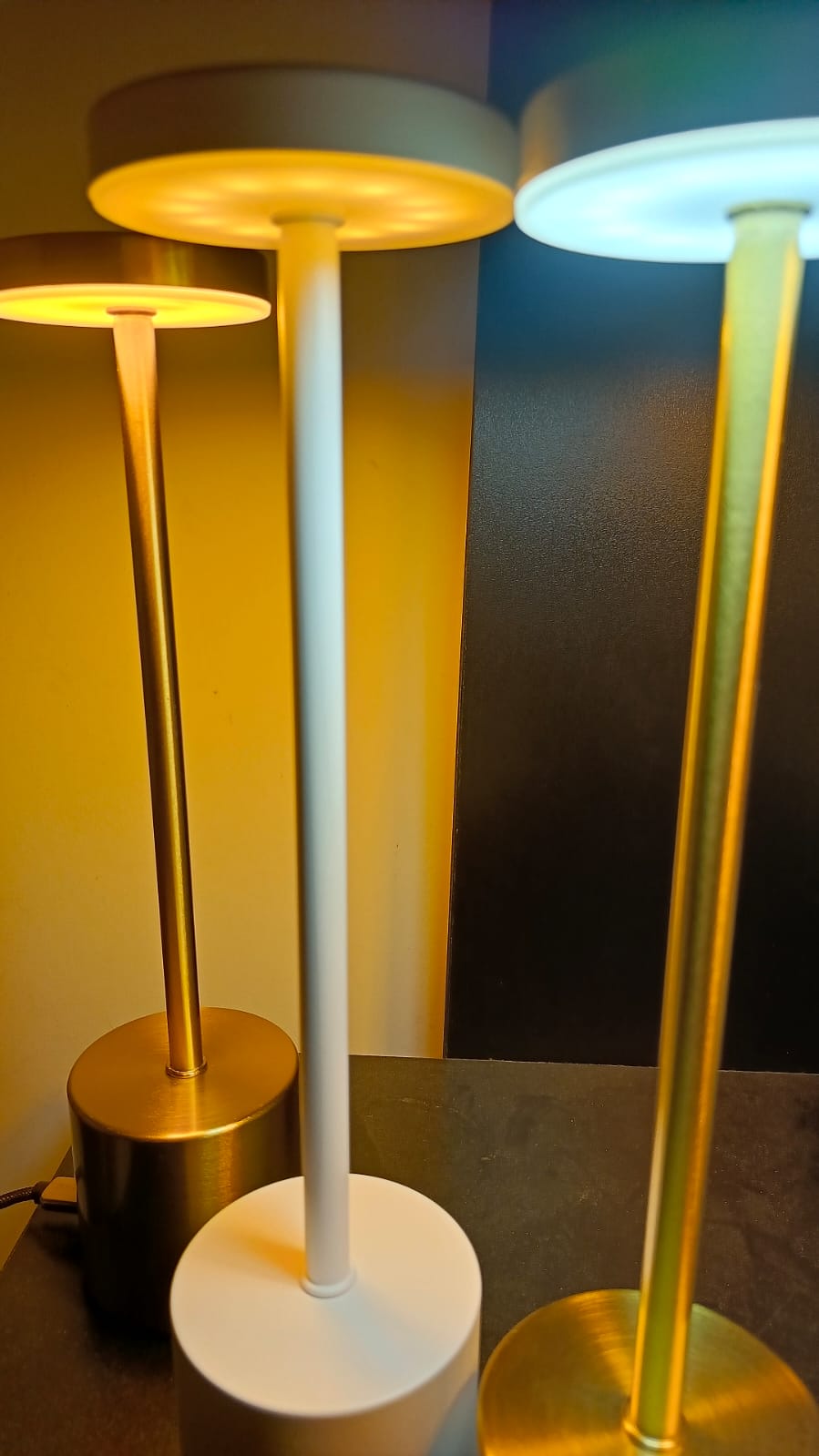 Three table lamps with different designs and colors on a reflective surface.