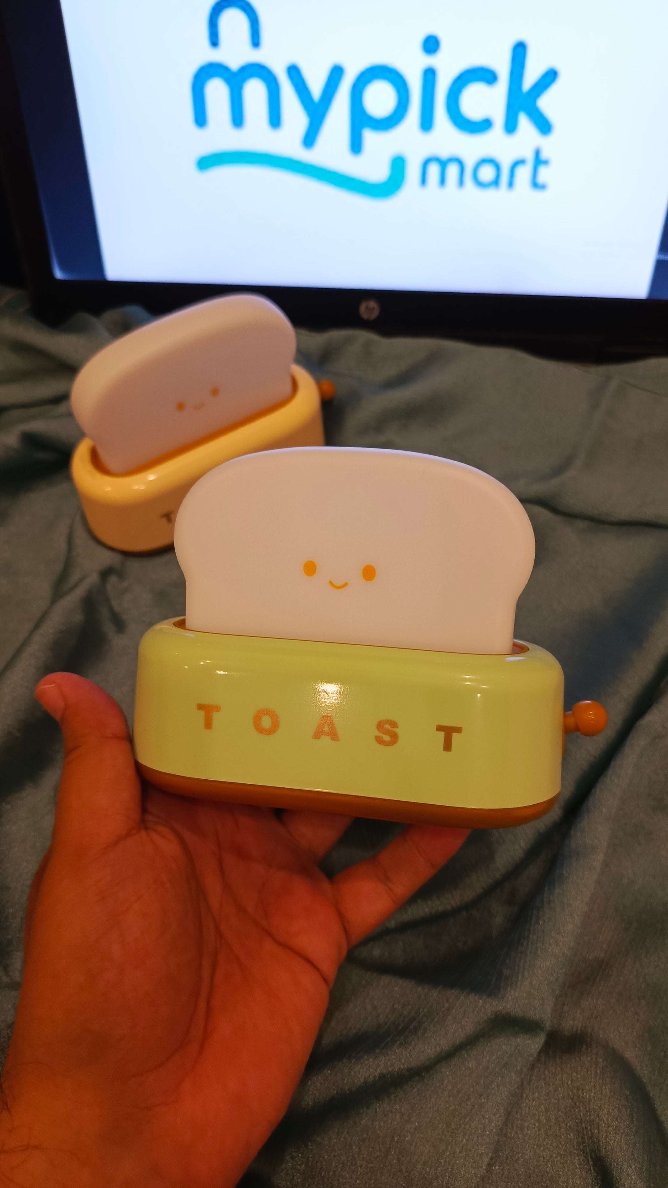 Small toaster toy held in a hand with a screen displaying 'mypick mart' in the background.