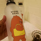 White water bottle with cartoon bear design and 'We Bare Bears' text, held against a tiled wall background.