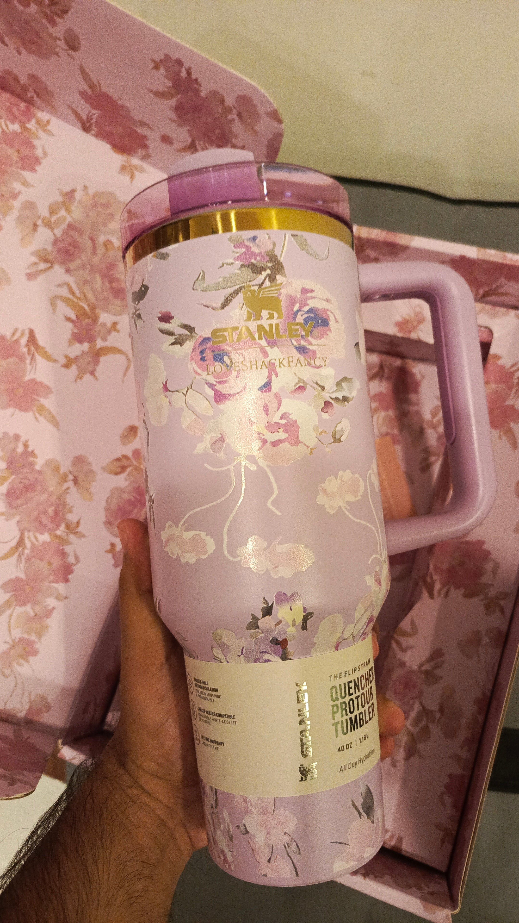 Tumbler with floral design and brand logo held against a floral background